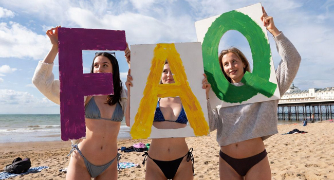 Tre partecipanti sulla spiaggia di Bournemouth tengono cartelli FAQ durante un soggiorno linguistico LISA! in Inghilterra