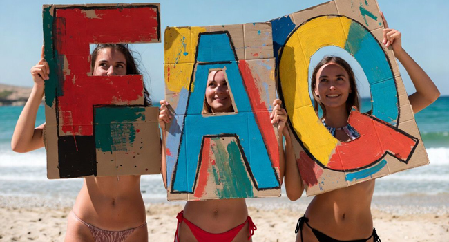 FAQ soggiorni linguistici LISA! – risposte alle domande frequenti Tre giovani donne sulla spiaggia tengono cartelli FAQ durante un soggiorno linguistico LISA!