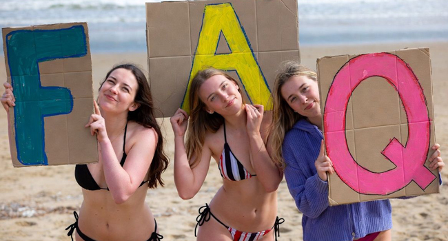  Tre partecipanti sulla spiaggia di Bournemouth tengono cartelli FAQ durante un soggiorno linguistico LISA! in Inghilterra