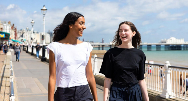 Soggiorni linguistici per adulti in Inghilterra Brighton con LISA! – lungomare, molo e mare Due partecipanti che passeggiano sul lungomare vicino al molo di Brighton durante un soggiorno linguistico LISA! in Inghilterra