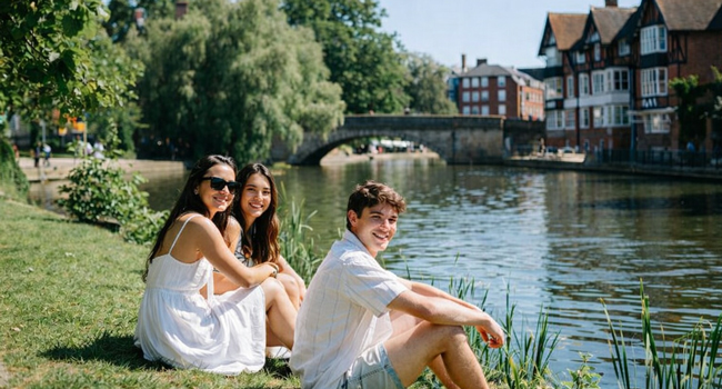 Adulti partecipanti a un soggiorno linguistico LISA! a Cambridge City Inghilterra seduti vicino al fiume godono del sole e del tempo libero