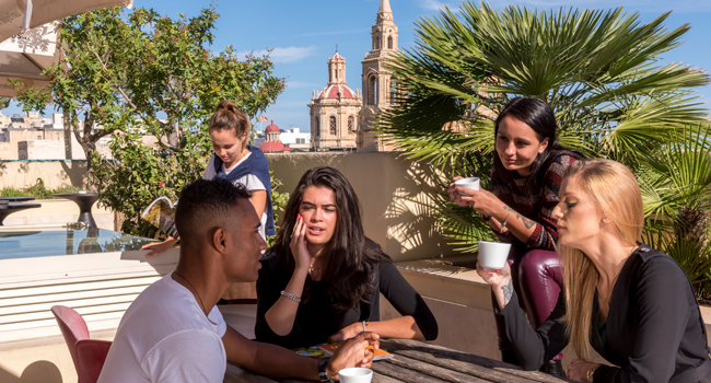Soggiorni linguistici a Malta per adulti con terrazza sul tetto a Sliema Partecipanti a un soggiorno linguistico per adulti a Malta sulla terrazza sul tetto della scuola di lingue a Sliema con vista sulla città