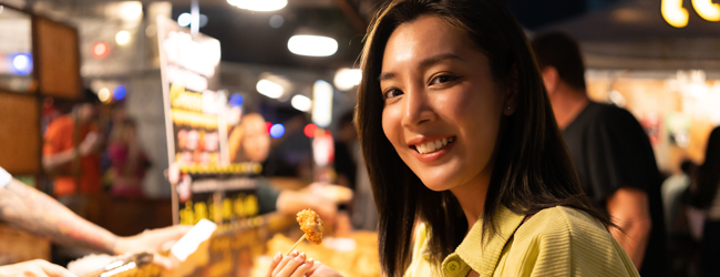 Mangiare fuori e uscire a Bangkok durante un soggiorno linguistico Una donna asiatica assaggia qualcosa in una bancarella di street food a Bangkok