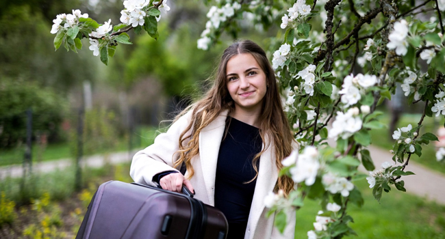 Prenotazione di un soggiorno linguistico LISA! – una ragazza con una valigia. Una ragazza con una valigia sotto un melo locale simboleggia la prenotazione di un soggiorno linguistico LISA!.