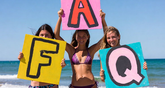 FAQ soggiorni linguistici LISA! – risposte alle domande frequenti Tre studentesse sulla spiaggia a Bournemouth tengono cartelli FAQ durante un soggiorno linguistico LISA!