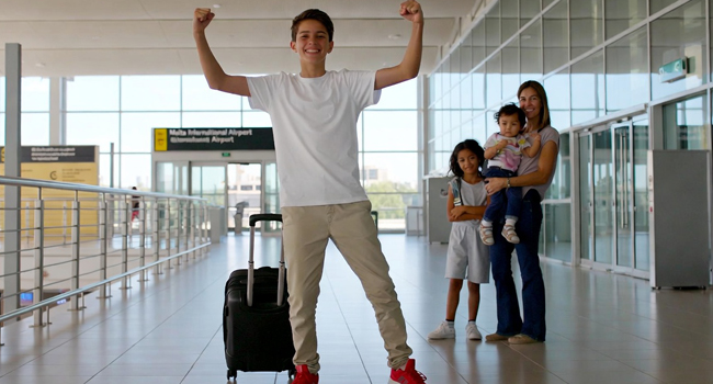 Arrivo a Malta per un soggiorno linguistico di inglese per studenti con LISA! Arrivo di uno studente a Malta per un soggiorno linguistico con le braccia alzate in posa di vittoria con genitori ospitanti sullo sfondo