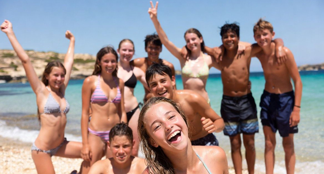 Programma di attività durante un soggiorno linguistico di inglese per studenti a Malta San Gwann con LISA! Dieci adolescenti sulla spiaggia a Malta San Gwann durante il programma di attività con le braccia alzate