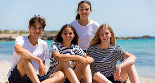 Soggiorni linguistici per studenti a Malta con LISA! – gruppo di studenti sulla spiaggia Quattro studenti seduti sulla spiaggia a Malta durante un soggiorno linguistico LISA! per studenti