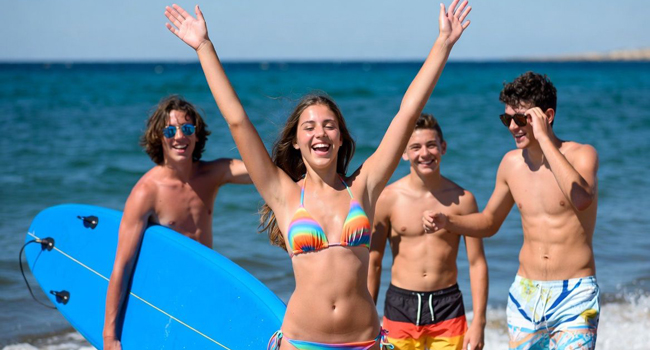 Sono qui, mamma: arrivata a un soggiorno linguistico a Malta con LISA! Ragazza alza le braccia con tre ragazzi e il mare sullo sfondo