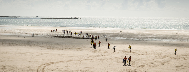 An einem breiten Sandstrand in Jersey sind viele Surfer mit Surfboard unterwegs