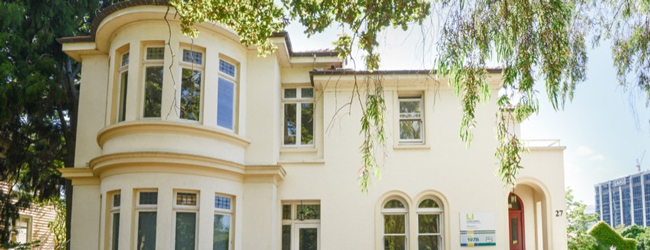 Hellgelbes Gebäude im Park als Sitz der LISA! Sprachschule in Auckland