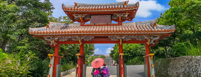 Eingangstor zum Shuri Schloss in Naha in Okinawa Zwei Damen in Kimono und Schirm gehen durch das Eingangstor zum Schloss Shuri