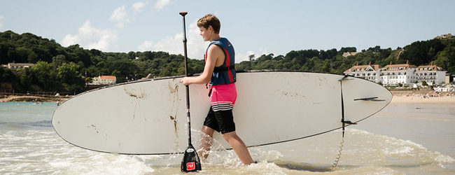 Ein Junge trägt ein Paddelboard ins Meer bei einer LISA! Schülersprachreise in Jersey