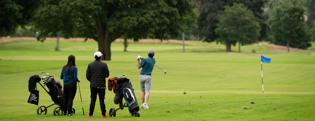 Jugendliche stehen auf einem Golfplatz und schauen beim Schlag zu