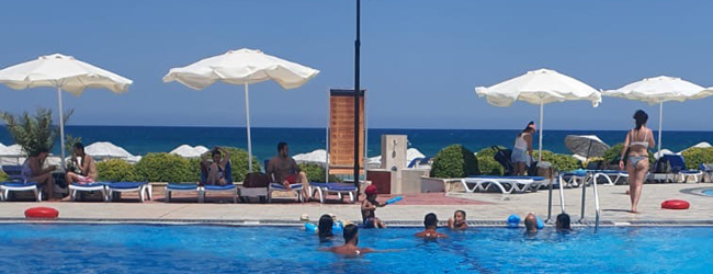 Poolspass am Meer bei einer Schülersprachreise in Nordzypern Menschen schwimmen im Pool und liegen auf Sonnenliegen, im Hintergrund das Meer in Nordzypern